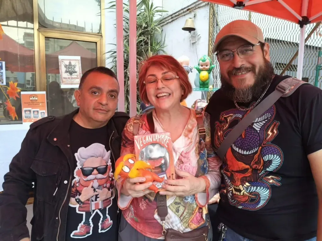 Tres coleccionistas sonriendo en la feria de creadores, uno de ellos sostiene un art toy naranja y una caja de figura de colección