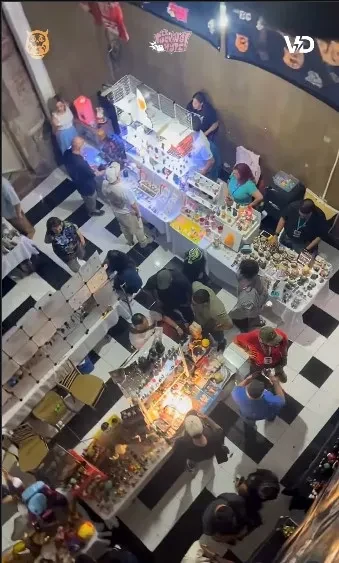Vista desde arriba de una feria con mesas de expositores, visitantes y piezas de colección