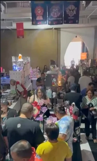 Pasillo de una feria lleno de visitantes recorriendo stands y mesas de expositores